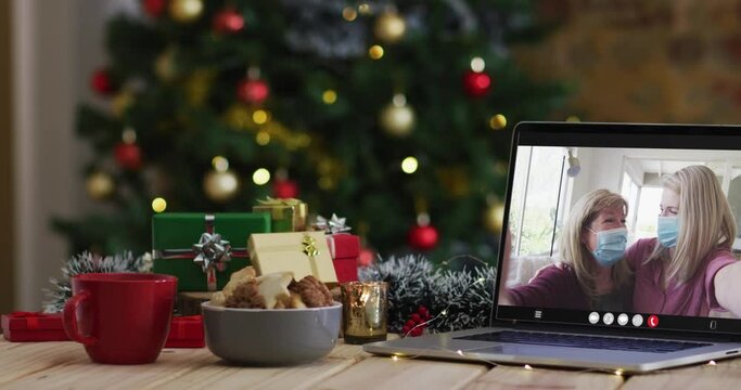 Mother and daughter in face masks on video call on laptop, with christmas tree