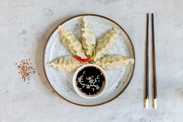 A portion of gyoza dumplings with soy sauce on a gray plate. On a gray stone background with chopsticks. Top view, copy of the space, horizontal