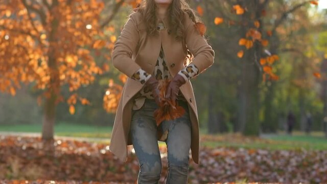 Hello autumn. smiling modern female in brown coat and yellow hat rejoicing outdoors in the city park in autumn.
