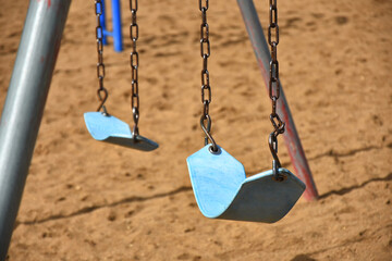 An image of two blue swing set seats in a children's playground. 