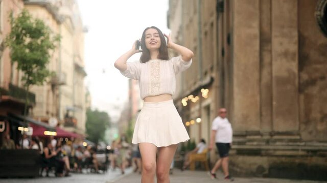 Happy cool woman wearing headphones dancing alone on street. Young adult happy girl sing and funny dancing in downtown very emotional. Modern lifestyle and happiness concept