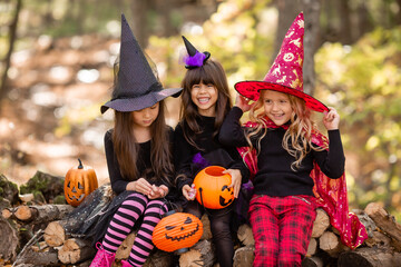 three little girls in witch costumes laugh, conjure, walk through the autumn forest with baskets for sweets in the shape of pumpkins. halloween concept, lifestyle . High quality photo