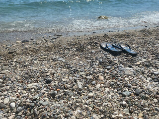 Blue flip-flops on the pebble beach with turquoise sea and blue sky in background. Summertime....