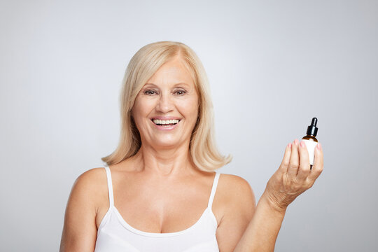 A happy blond senior lady trying out new serum. Beauty photography