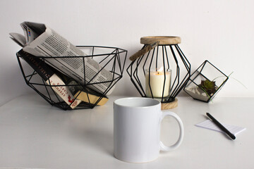 Fototapeta na wymiar white cup mockup on a background of plants newspaper, candle and pen on a white table