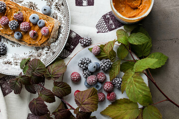 Peanut butter sandwich on a vintage plate on the table with flowers and leaves. Frozen various berries for lunch. Light breakfast.