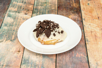 White chocolate cinnamon roll with cookie pieces on wooden table