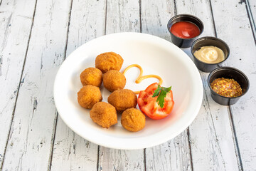 serving of round chicken croquettes with tomato and tomato sauces, mayonnaise and dijon mustard to...