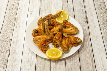 Portion of chicken wings fried in olive oil with lemon to marinate on a white plate