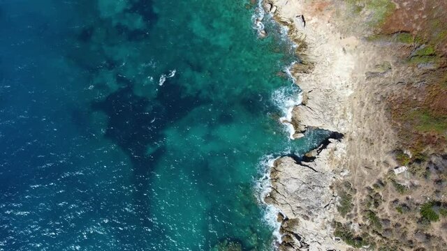 Aerial drone view of sea waves breaking on rocks at shore. Beautiful natural rocky beach at summer. Ocean waves crushing on wild beach at sunset. Coastline.