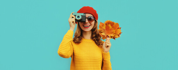 Autumn portrait of happy smiling young woman with film camera and yellow maple leaves wearing a...