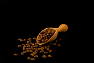 Coffee beans in a wooden scoop isolated on a black background. Roasted coffee beans isolated. A wooden scoop with coffee.