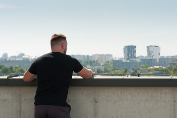 A young man standing on the roof of a high-rise building looking at the panorama of the city