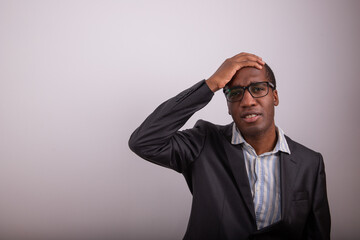 African businessman has a confused expression, he puts his hand on his head and is disoriented. Man...