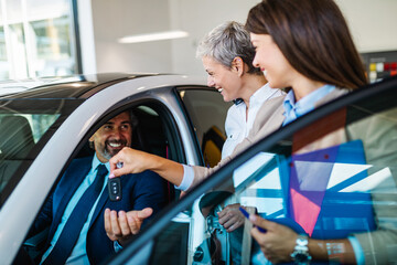 Handsome senior man buying a new car at the car showroom.