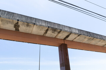 Elevated street, concrete sections atop an orange central support, dark metal upright support and electrical lines against blue sky, horizontal aspect
