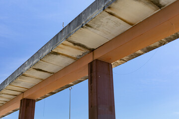 Concrete roadway on a single central support seen from underneath, isolated against blue sky, horizontal aspect