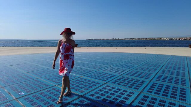 Woman with hat walking in Zadar chronicles by the Adriatic Sea in Croatia and Dalmatia region. Panoramic view of solar panels on the seafront and monument to the sun.