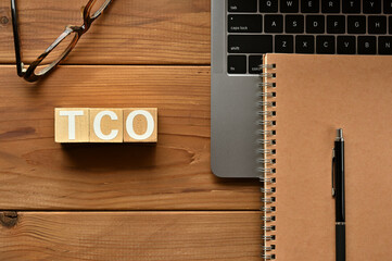 On the table there is a word cube lined TCO with laptop computers and glasses. It is an...