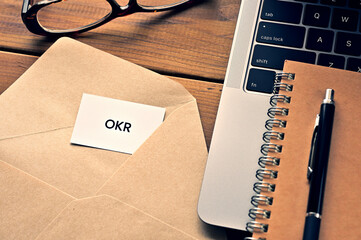 There is a laptop, a pen, an envelope, and a card with OKR which is an abbreviation for Objectives...