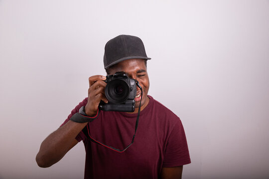 Photographer takes a picture while looking through the camera viewfinder. African photographer isolated on white background. Photograph taken in the studio. Professional Photographer concept.