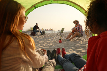 Friends resting on sandy beach. View from camping tent