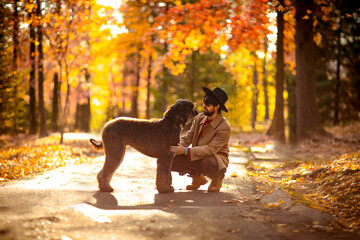 a handsome, brutal man in a coat and hat, walking in the park during the day, in autumn, with a...