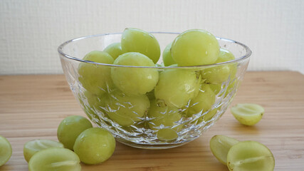 木目のテーブルの中心に置かれたガラスのお皿に盛られたシャインマスカット