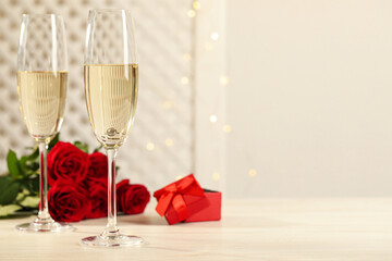 Beautiful engagement ring with gemstone in glass of sparkling wine and roses on white wooden table....