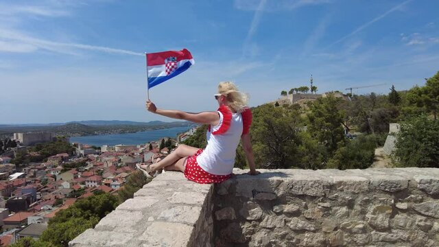 Woman on the walls of Barone Fortress with Croatian flag on Sibenik cityscape. View of St. Michael castle and St. John's Fort. Sibenik historic city of Croatia in Dalmatia.