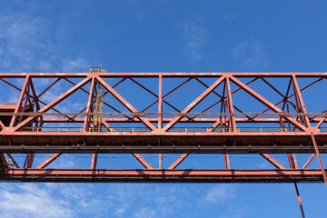 Overhead industrial structure painted red, isolated against a vivid blue sky, horizontal aspect