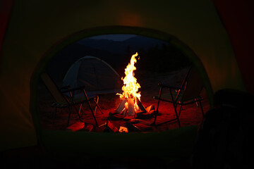 Beautiful bonfire and folding chairs outdoors in evening, view from camping tent