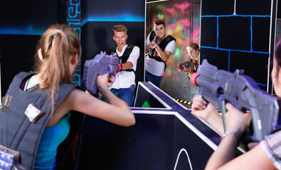 Two cheerful laser tag teams playing enthusiastically and aiming at each other in dark room