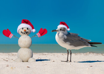 Snowman and Seagull on the beach. Sandy Christmas snowman and Seagull bird in red Santa hat at the...