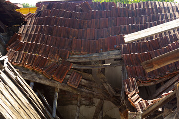 old and weathered crumbling roof with fallen rafters and broken tiles falling down from an abandoned house in a countryside