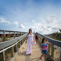Slightly overweight mother with white Swimsuit Coverup and  two female children at a wood platform to the beach over the sand dunes