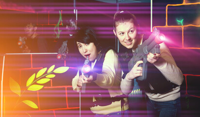Portrait of two emotional female laser tag players having fun in multinational team on laser tag arena.