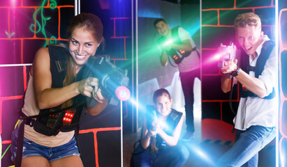 Group of young positive people playing enthusiastically lasergames in dark room
