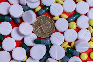 One pound coin against a background of many white, yellow pills and medicinal capsules without any names or logos