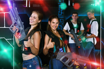 Fototapeta na wymiar Portrait of two cheerful girls with laser pistols in their hands in dark laser tag room