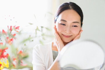 鏡を見てスキンケアをする女性（ビューティーイメージ）
