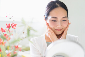 鏡を見てスキンケアをする女性（ビューティーイメージ）