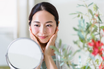 鏡を見てスキンケアをする女性（ビューティーイメージ）