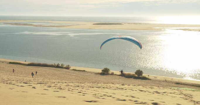 Paragliding Activity - Paraglider Take Off At Grande Dune du Pilat With Sunlit Waters Of Arcachon Bay In France, Europe. - wide shot