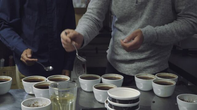 Two men dipping spoons in cups at coffee tasting and cupping session