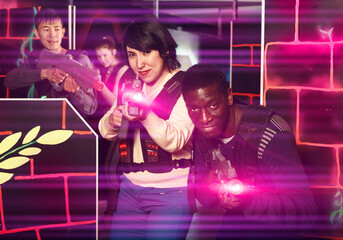 Portrait of young man and woman with the laser pistols playing laser tag on dark labyrinth