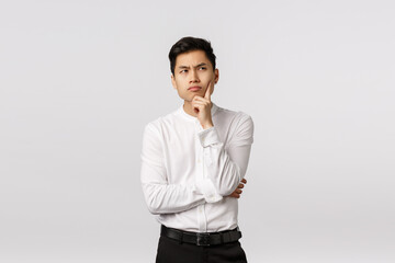 Handsome asian businessman trying understand meaning of life, touching chin, looking up with serious focused expression, thinking up business concepts, searching inspiration, pondering choices - obrazy, fototapety, plakaty