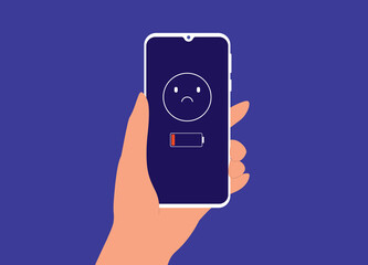 A Person's Hand Holding Smartphone With Low Battery And Sad Emoji Icon Showing Up On The Device Screen.