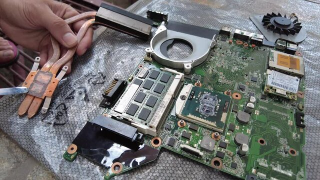 Replacing the thermal paste of an old laptop motherboard by scraping it off first from the heatsink and placing it with a new one. The laptop motherboard is experiencing overheating issues.