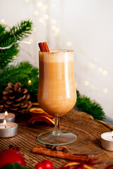 A glass of traditional Christmas drink eggnog on a festive table, vertical photo. Spicy drink made from egg and milk with cinnamon, cardamom.